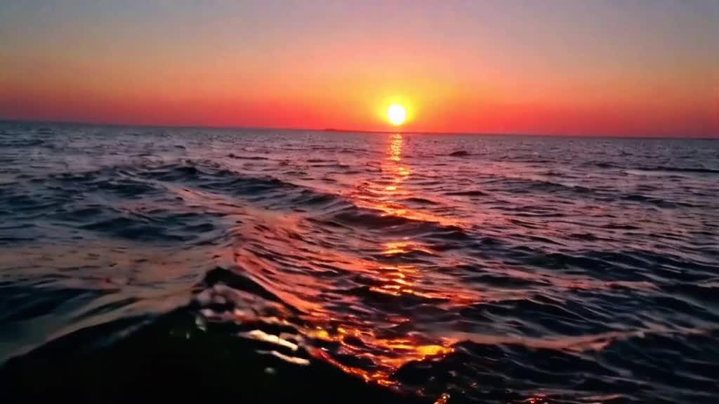 夕阳西下时宁静辽阔海洋的画面。天空被柔和的粉红色和橙色色调所描绘。相机缓缓向下移动至地平线,太阳在那里即将落山。随着光线的消逝,一声最后的“唵”声充满了空间,象征着灵魂永恒的安息。