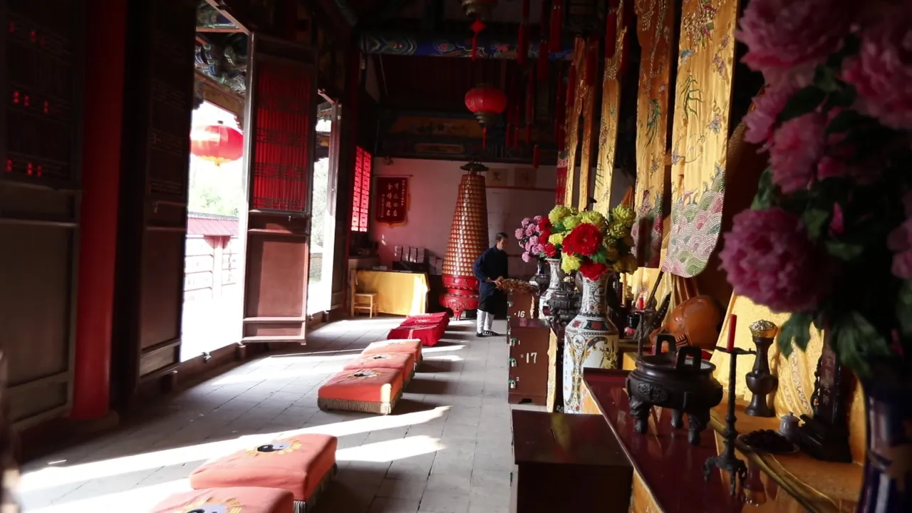 传统寺庙大殿内部实景，僧人整理供桌与红色蒲团